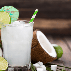 Brazilian coconut cocktail with straw, mini umbrella, and lime wedges