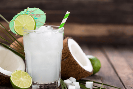 Brazilian coconut cocktail with straw, mini umbrella, and lime wedges
