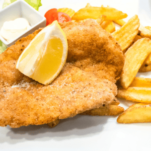 Chicken milanesa with a lemon wedge and fried potatoes