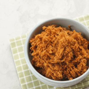 Shredded carne seca in a white bowl on tea towel