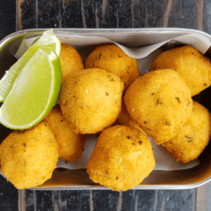 fried fish balls served with wedges of lime in a silver tray.