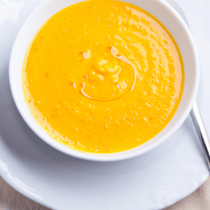 A bowl of bright orange honeynut squash soup on a white plate.