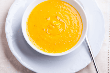 A bowl of bright orange honeynut squash soup on a white plate. 