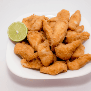 frango a passarinho, brazilian fried chicken, piled on a white dish with a lime wedge garnish